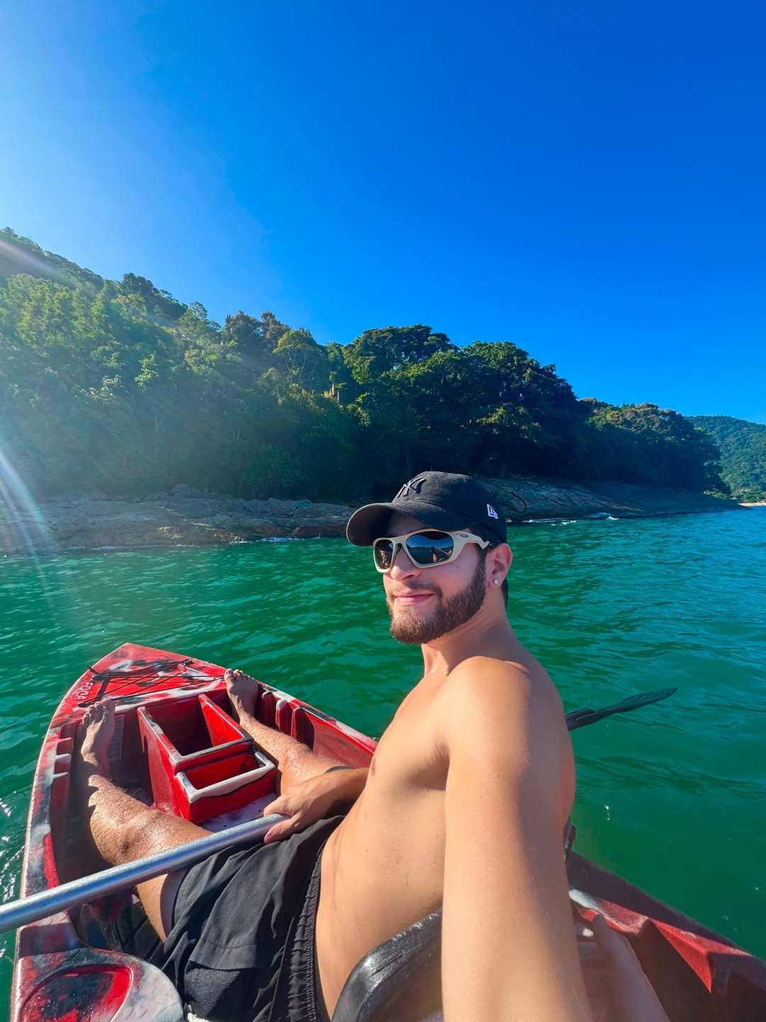 O Vagner de boné e óculos escuros, numa canoa vermelha, num mar verde entre morros de mata.
