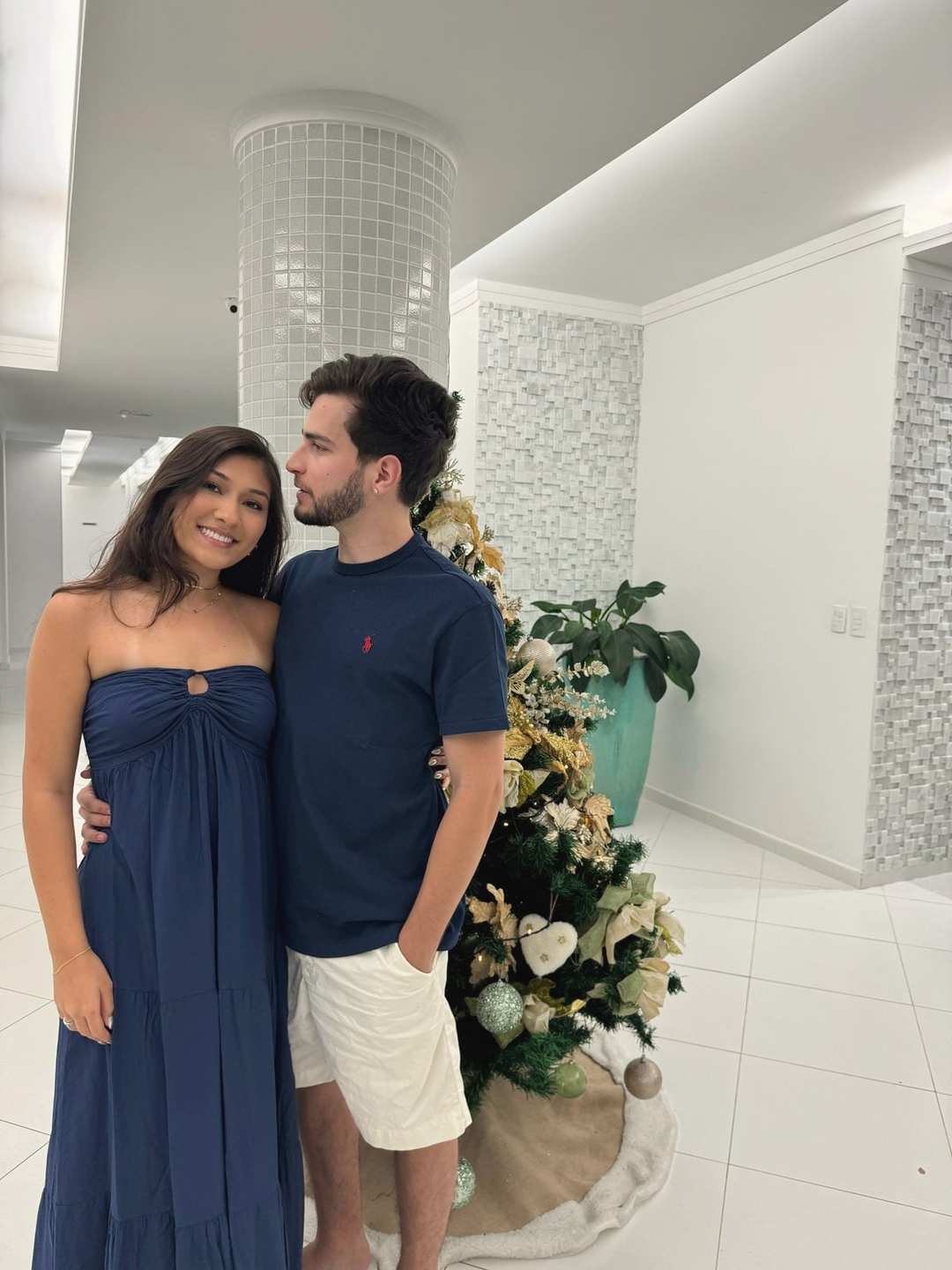 O Vagner e a mulher, arrumados, ao lado de uma árvore de Natal.