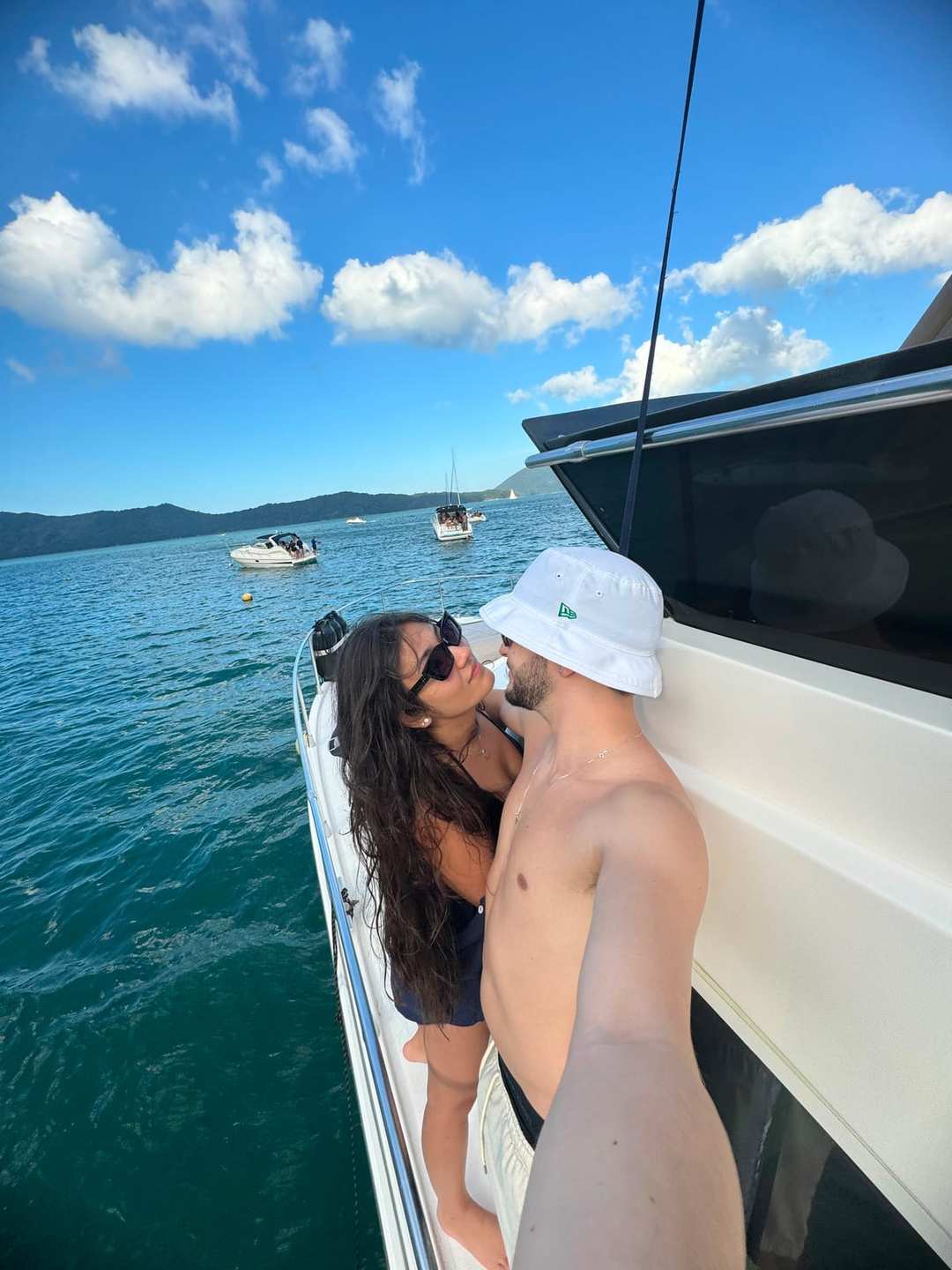 O Vagner e a mulher numa lancha branca, num mar azul com morros ao fundo.