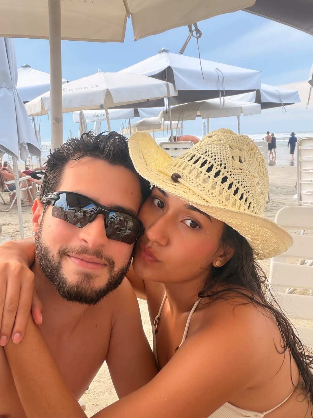 O Vagner de óculos escuros com a mulher de chapéu de palha, numa praia.