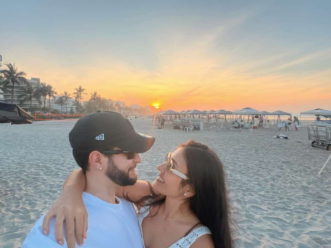O Vagner abraçado com a mulher numa praia, no pôr do sol.